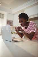 Woman using laptop while having coffee in kitchen