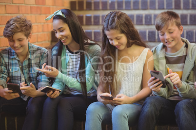 Group of smiling school friends sitting on staircase using mobile phone