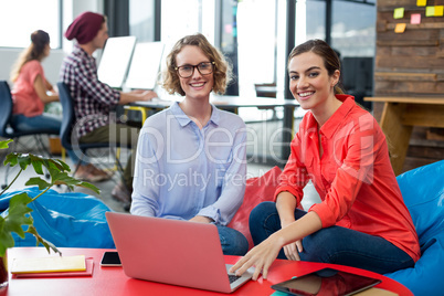 Smiling business executives sitting in office with laptop on table