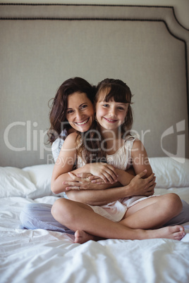 Smiling mother embracing her daughter in bedroom