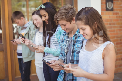 Group of smiling school friends using mobile phone in corridor