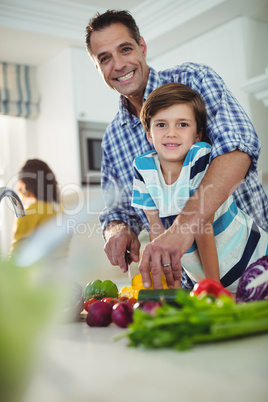 Portrait of father and son chopping vegetables in kitchen