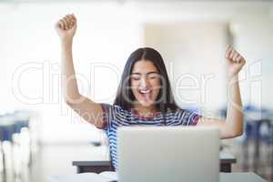 Excited schoolgirl sitting with laptop in classroom