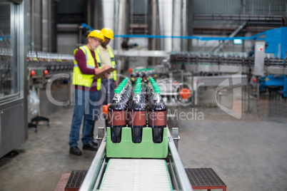 Two factory workers monitoring cold drink bottles on production line