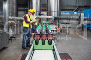 Two factory workers monitoring cold drink bottles on production line