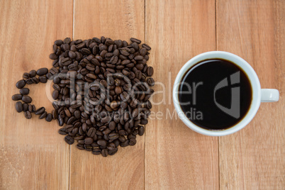 Cup of black coffee and coffee beans forming shape of cup