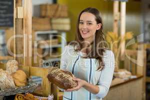 Portrait of smiling female staff holding a round loaf of bread at counter