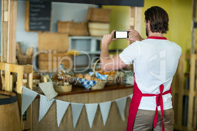 Rear view of bakery staff photographing bakery snacks and bread on the counter