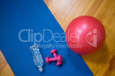 Fitness ball, water bottle, dumbbell and exercise mat on wooden floor