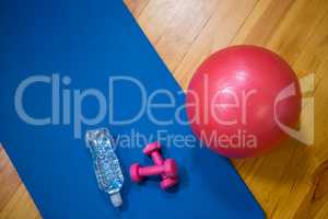 Fitness ball, water bottle, dumbbell and exercise mat on wooden floor