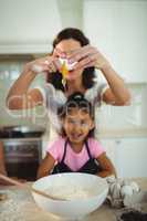 Mother and daughter breaking egg in bowl while preparing cookie