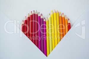 Colored pencils arranged in heart shape on white background