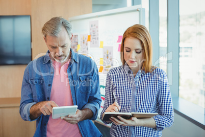 Male executive using digital tablet while female executive noting on diary