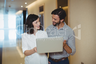 Male and female executives using laptop in corridor