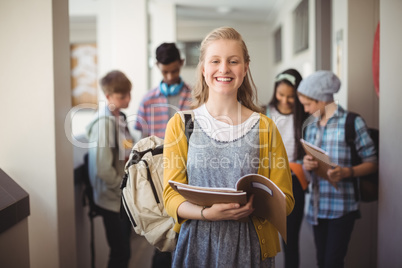Portrait of smiling schoolgirl standing with notebook in corridor