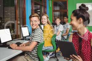 Smiling students studying on digital tablet and computer in classroom