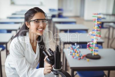 Portrait of happy schoolgirl holding microscope in laboratory