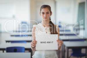 Schoolgirl holding white paper with text sign in classroom