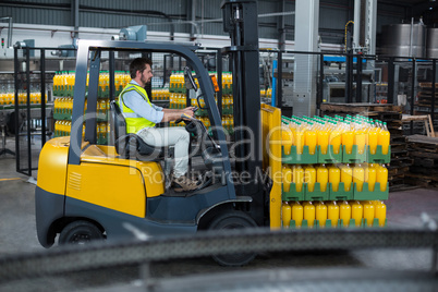 Factory worker loading packed juice bottles on forklift