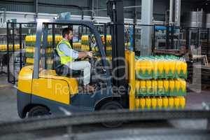 Factory worker loading packed juice bottles on forklift