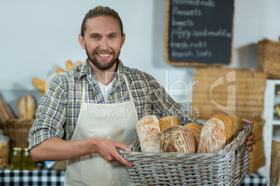 Portrait of smiling male staff holding a basket of baguettes at counter