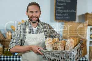 Portrait of smiling male staff holding a basket of baguettes at counter