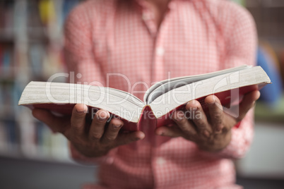 Mid section of school teacher holding book in library