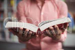 Mid section of school teacher holding book in library