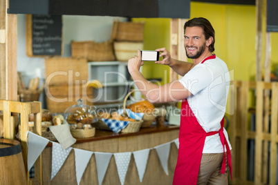 Portrait of bakery staff photographing bakery snacks and bread on the counter