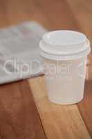 Close-up of disposable coffee cup and newspaper
