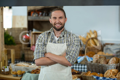 Portrait of smiling male staff standing with arms crossed at counter