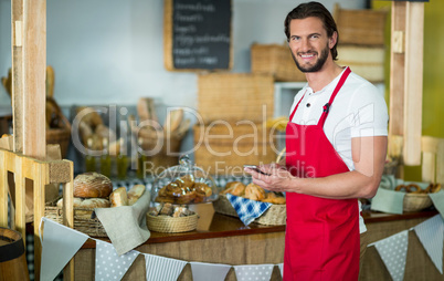 Portrait of smiling bakery staff using mobile phone at counter