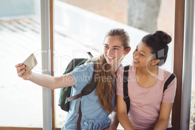 Happy schoolgirls taking selfie on mobile phone in corridor