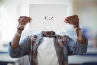 Schoolboy holding white paper with text sign in classroom