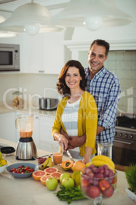 Happy couple embracing while preparing smoothie in kitchen