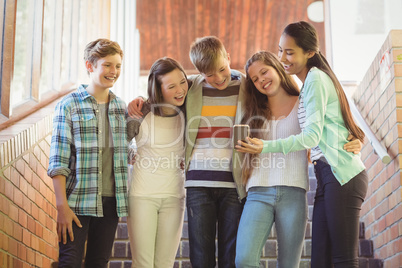 Smiling school students standing on the staircase using mobile phone