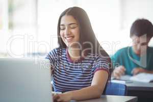 Happy schoolgirl using laptop in classroom