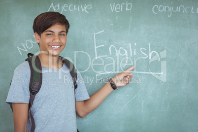 Portrait of happy schoolboy pointing at chalkboard in classroom