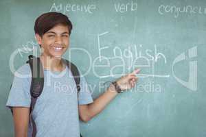 Portrait of happy schoolboy pointing at chalkboard in classroom