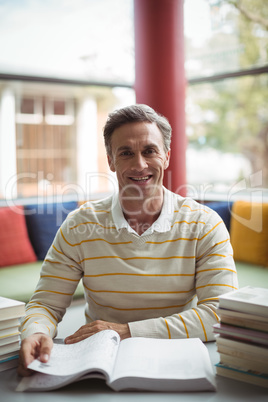Portrait of happy school teacher reading book in library