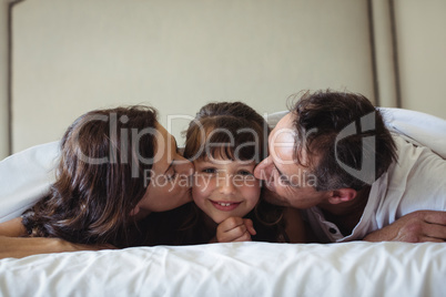 Parents kissing their daughter on cheek in bedroom