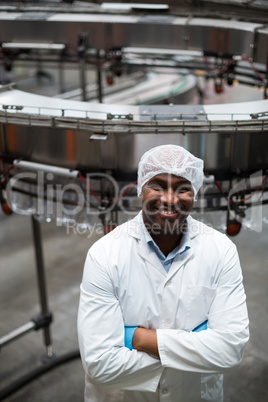 Smiling factory engineer standing with arms crossed in bottle factory