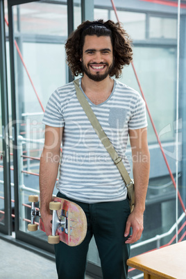 Smiling graphic designer with skateboard standing in creative office