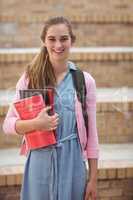 Portrait of schoolgirl standing with schoolbag and books in campus