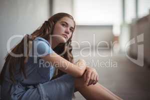 Thoughtful schoolgirl sitting in corridor