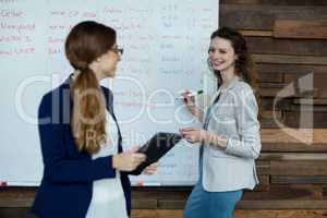 Business executive writing on white board while interacting with a woman