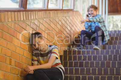 School friend bullying a sad boy in school corridor