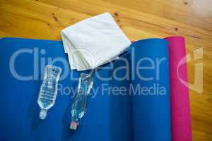 Exercise mat, towel and water bottles kept on wooden floor