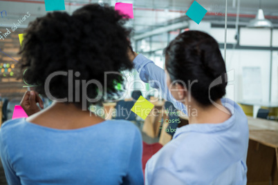 Female graphic designer pointing to the sticky notes on the glass in creative office