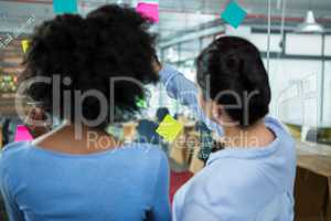 Female graphic designer pointing to the sticky notes on the glass in creative office